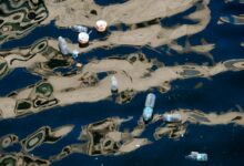 Floating plastic bottles and trash polluting a waterway with reflections.