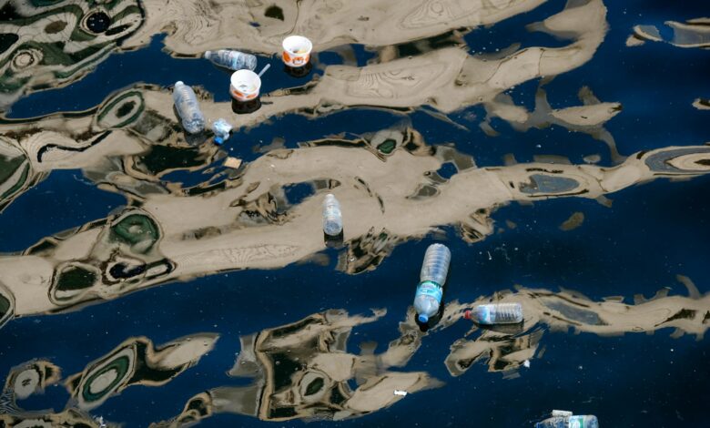 Floating plastic bottles and trash polluting a waterway with reflections.