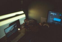 Dark room with a laptop and gaming console creating a moody tech atmosphere.