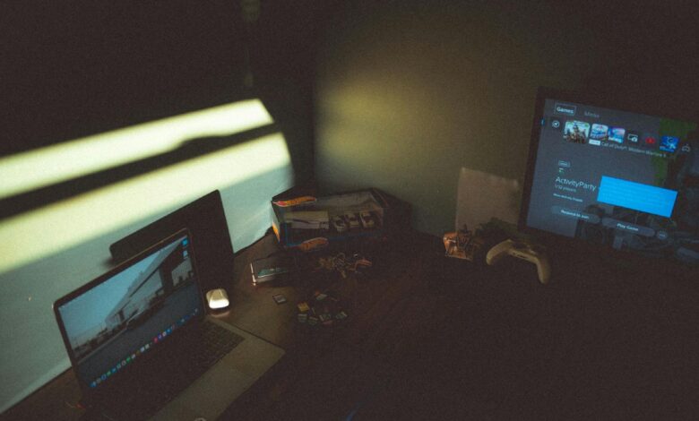 Dark room with a laptop and gaming console creating a moody tech atmosphere.