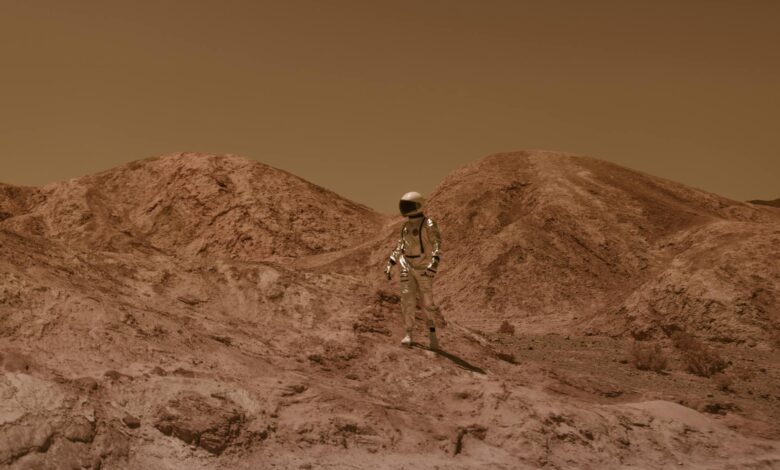 Astronaut in spacesuit explores barren, Mars-like desert terrain under brown sky.