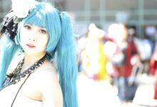 Vibrant cosplay portrait of a woman with blue hair and intricate costume in bright outdoor setting.