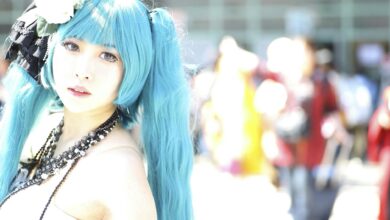 Vibrant cosplay portrait of a woman with blue hair and intricate costume in bright outdoor setting.