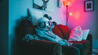 Anonymous guy in VR helmet sitting on sofa with controller while playing video game in cozy room with dark light