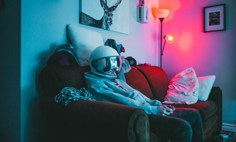 Anonymous guy in VR helmet sitting on sofa with controller while playing video game in cozy room with dark light
