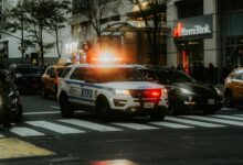 NYPD patrol car with flashing lights in downtown city traffic scene.