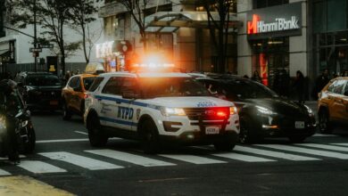 NYPD patrol car with flashing lights in downtown city traffic scene.