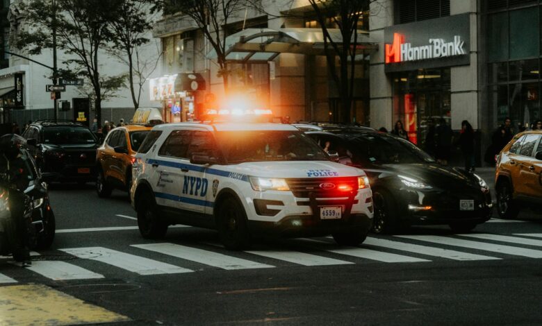 NYPD patrol car with flashing lights in downtown city traffic scene.