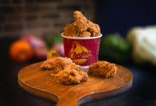 Mouth-watering fried chicken in a bucket displayed beautifully with blurred vegetables in the background.