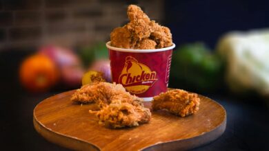 Mouth-watering fried chicken in a bucket displayed beautifully with blurred vegetables in the background.