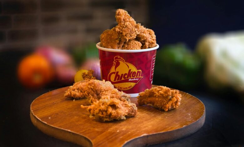 Mouth-watering fried chicken in a bucket displayed beautifully with blurred vegetables in the background.