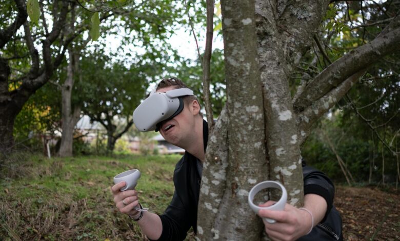 Person using VR headset and controllers in a wooded outdoor setting.