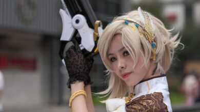 Cosplayer with intricate costume and prop gun, posing outdoors during the day.