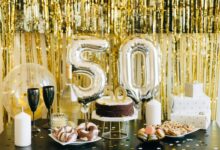 Stylish 50th birthday party setup with cake, gifts, and balloons in gold theme.