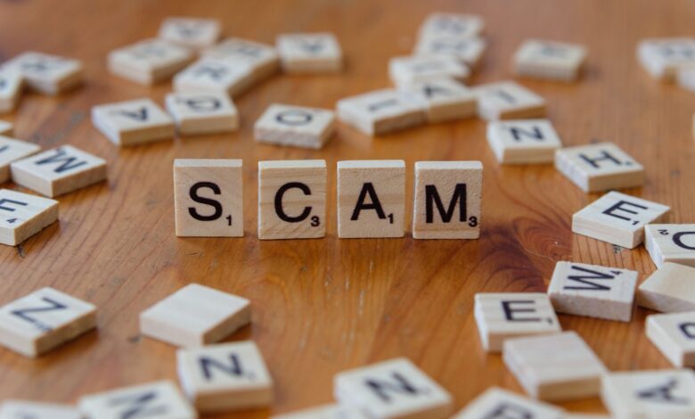 Image of Scrabble tiles spelling 'scam' surrounded by scattered letters on a wooden table.