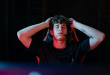 Young man with headset and tattoos, taking a break from gaming with eyes closed, seated indoors.