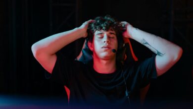 Young man with headset and tattoos, taking a break from gaming with eyes closed, seated indoors.