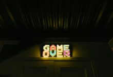 Glowing neon sign with pixelated Game Over text in a dark arcade setting.
