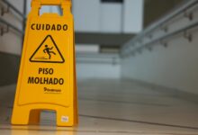 Yellow caution wet floor sign with Portuguese text in an indoor hallway.