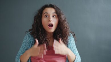 A surprised woman expressing emotion indoors with a gray background.