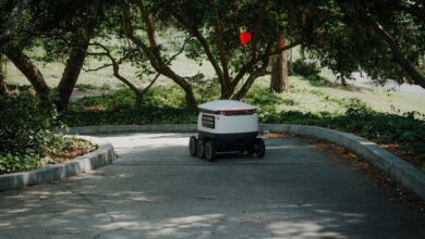 An autonomous delivery robot moves through a shaded pathway in a park, exemplifying modern logistics.