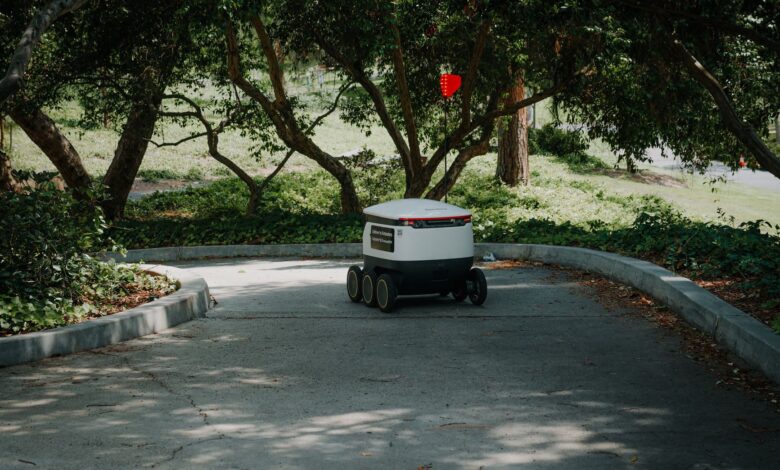 An autonomous delivery robot moves through a shaded pathway in a park, exemplifying modern logistics.