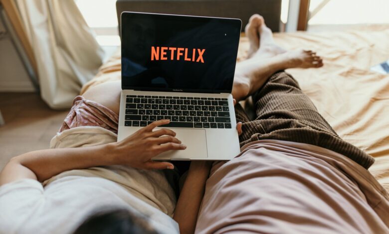 A couple lying comfortably in bed watching Netflix on a laptop, enjoying leisure time together indoors.