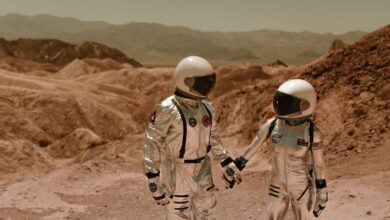 Two astronauts in spacesuits exploring a barren, sci-fi landscape.