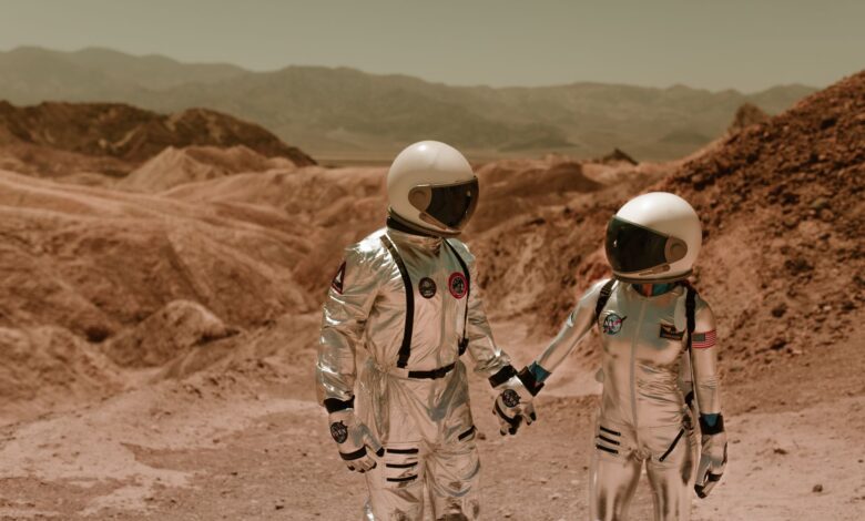 Two astronauts in spacesuits exploring a barren, sci-fi landscape.