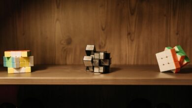 A collection of various Rubik's cubes displayed on a wooden shelf, showcasing unique designs and patterns.