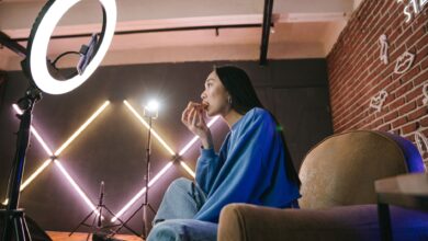Asian woman content creator eating pizza while recording a video indoors with ring light.