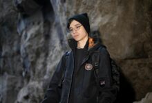 A young adult in a black jacket and beanie inside a rocky cave.