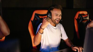 A man celebrating a win in a gaming chair, wearing headphones and using a PC.