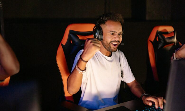A man celebrating a win in a gaming chair, wearing headphones and using a PC.