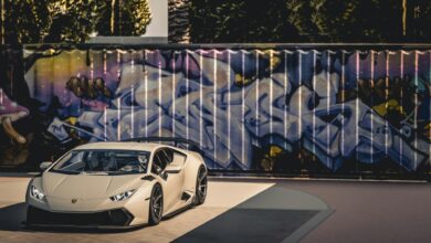A sleek luxury sports car parked in front of a vibrant graffiti wall under bright daylight.