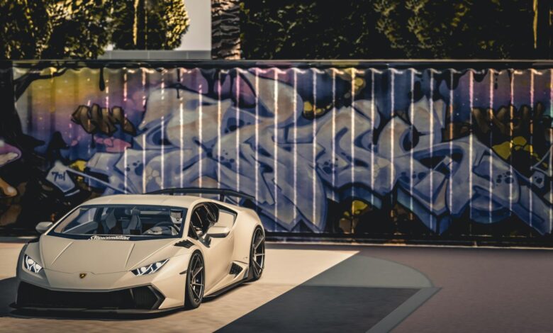 A sleek luxury sports car parked in front of a vibrant graffiti wall under bright daylight.