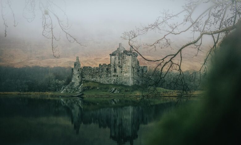 A fog-laden medieval castle with a reflection in a misty lake creates an eerie and historic scene.