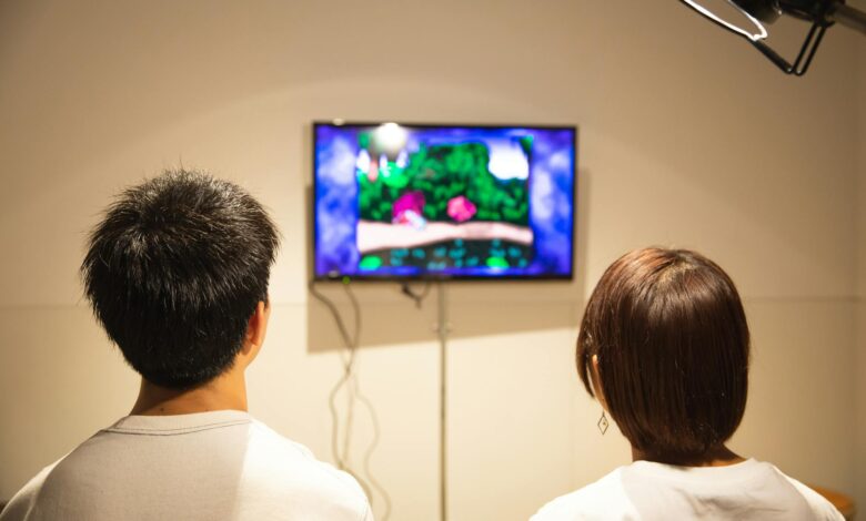 Back view of anonymous young guy and lady in white t shirts sitting in living room and playing video game