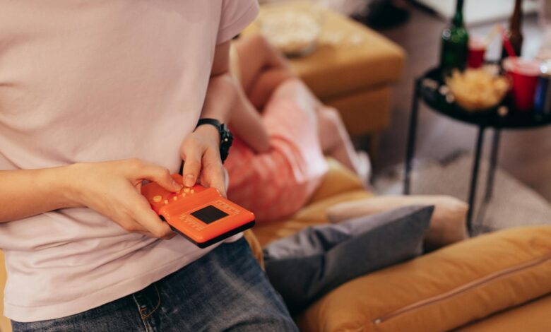 Person playing handheld game on couch, surrounded by relaxed setting with snacks.