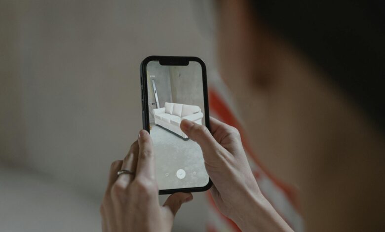 Person using augmented reality on smartphone to visualize a sofa in a room.