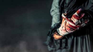 Surreal image of a woman's bloodied, bandaged hand in dark ambiance.