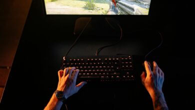 A gamer intensely playing a first-person shooter game on a computer setup indoors at night.