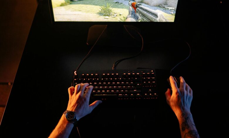 A gamer intensely playing a first-person shooter game on a computer setup indoors at night.
