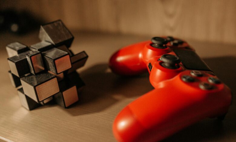 Close-up of a red game controller and 3D cube puzzle on a wooden surface.