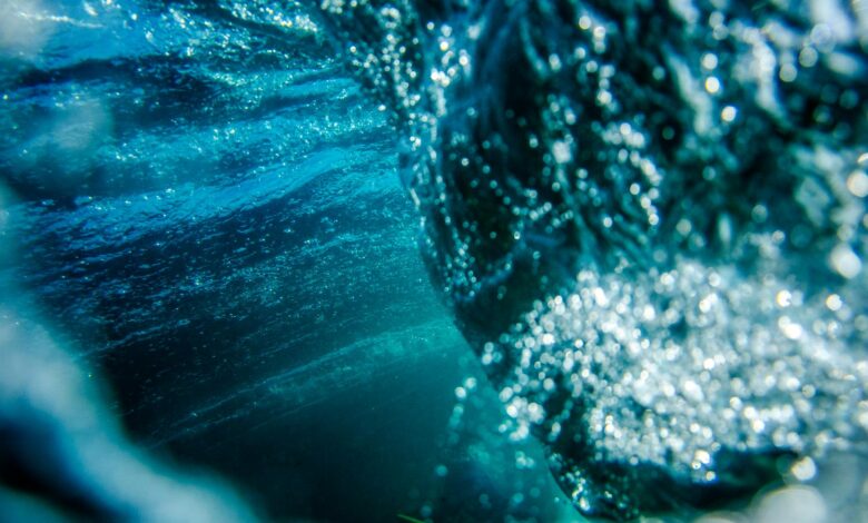 Underwater shot of unrecognizable object diving deep and making bubbles and waves during process