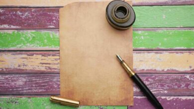Flat lay of vintage paper with ink bottle and pen on a colorful wooden surface.