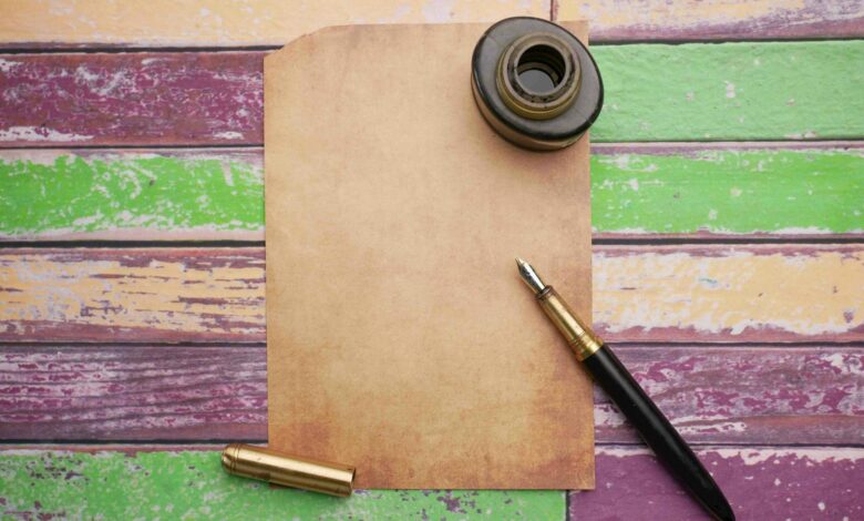 Flat lay of vintage paper with ink bottle and pen on a colorful wooden surface.