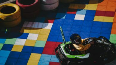 Child in go-kart racing on colorfully tiled track surrounded by tires.