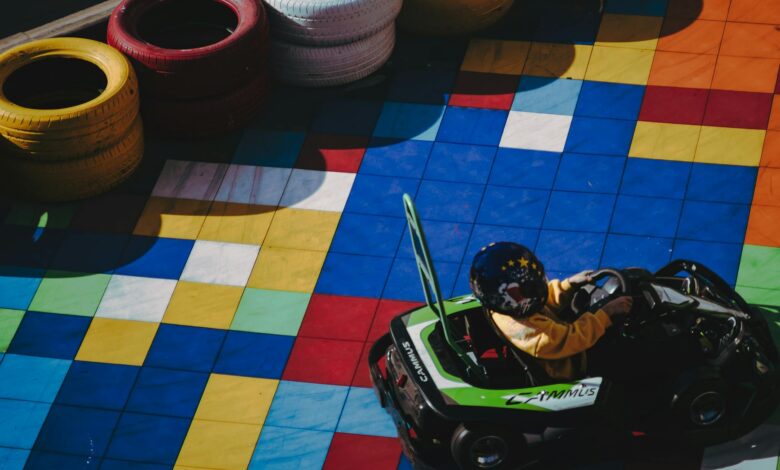 Child in go-kart racing on colorfully tiled track surrounded by tires.