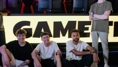 Four young men posing confidently in an eSports arena with gaming setups in the background.